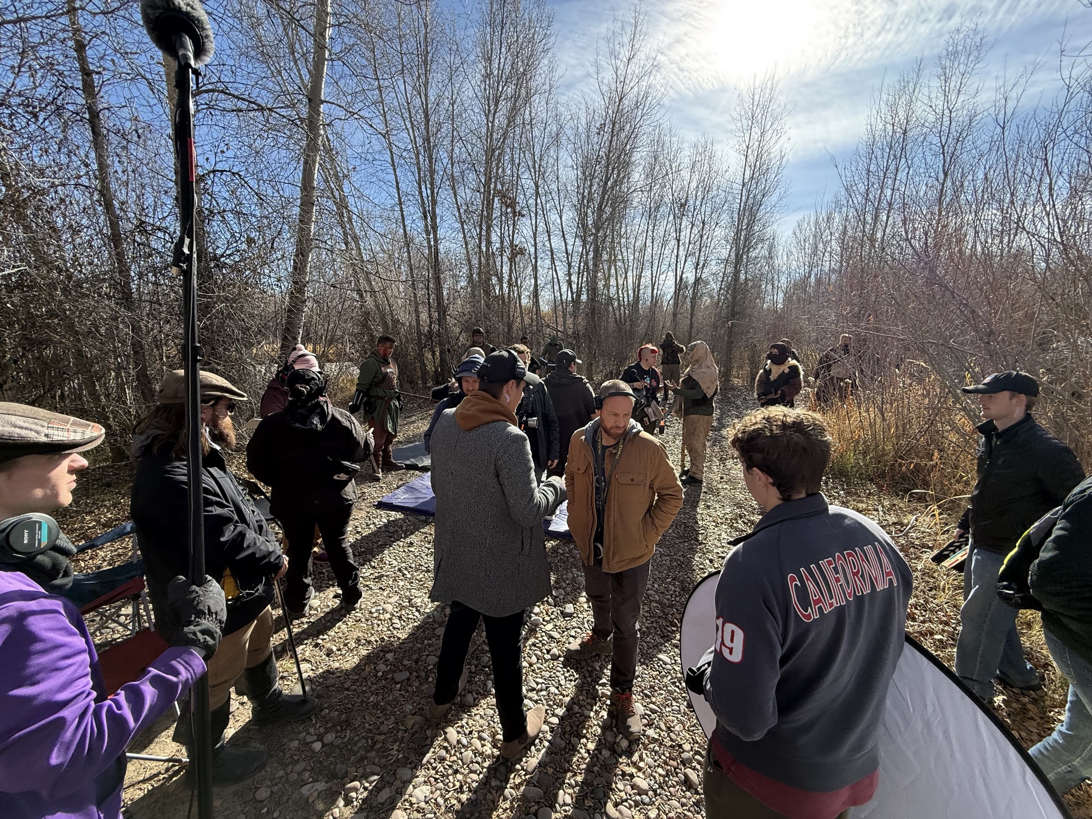 Large film crew staging a forest scene with audio and reflectors
